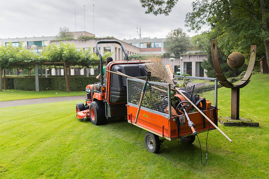 Dans les jardins de La Combe, un tracteur pour couper l'herbe avec sa remorque se déplacent