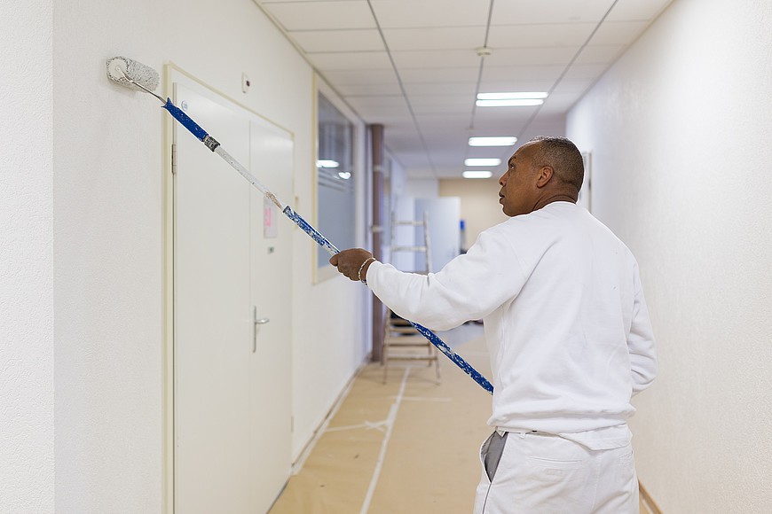 Un homme peint les murs en blanc dans un couloir
