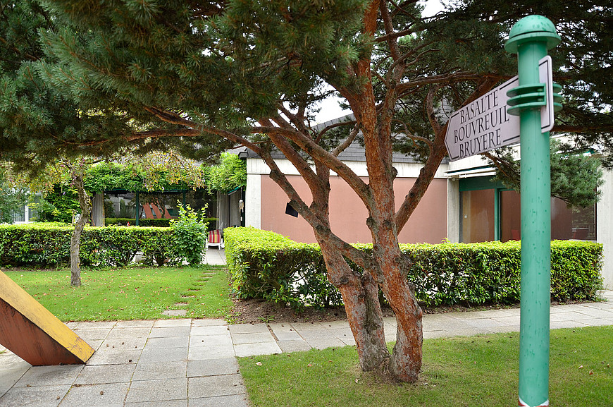 Jardin de la combe avec un arbre au centre et un écriteau indiquant les appartements