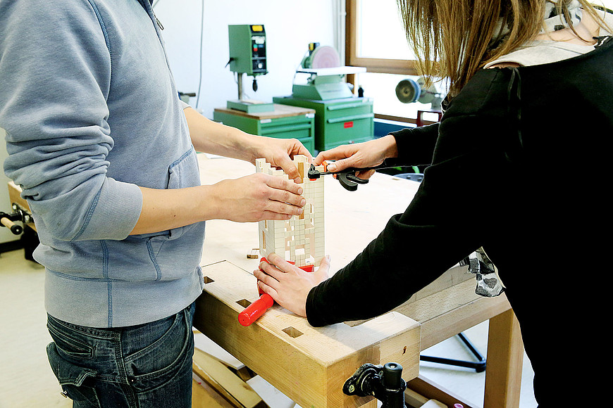 Deux personnes travaillent autour d'un élément en bois qui ressemble à une petite tour